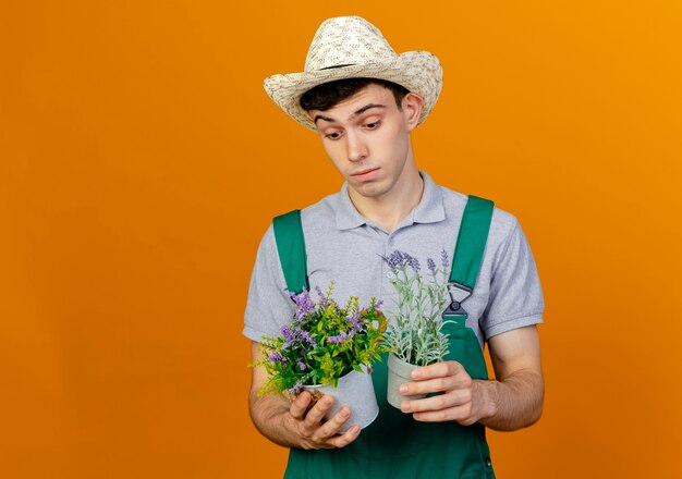 Смущенный молодой мужчина-садовник в садовой шляпе держит цветы в цветочном горшке