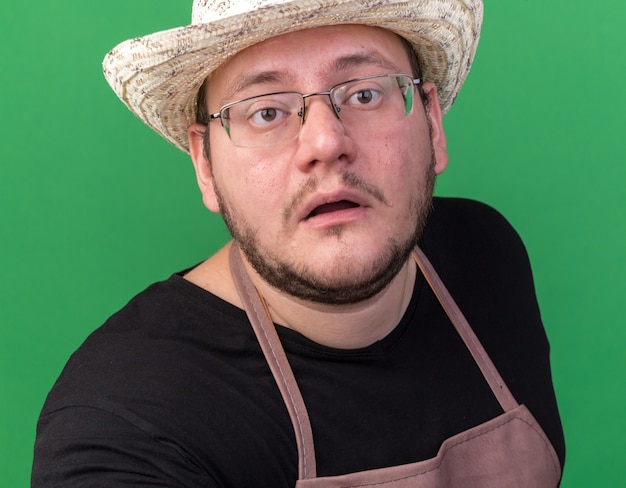 Confused young male gardener wearing gardening hat isolated on green wall