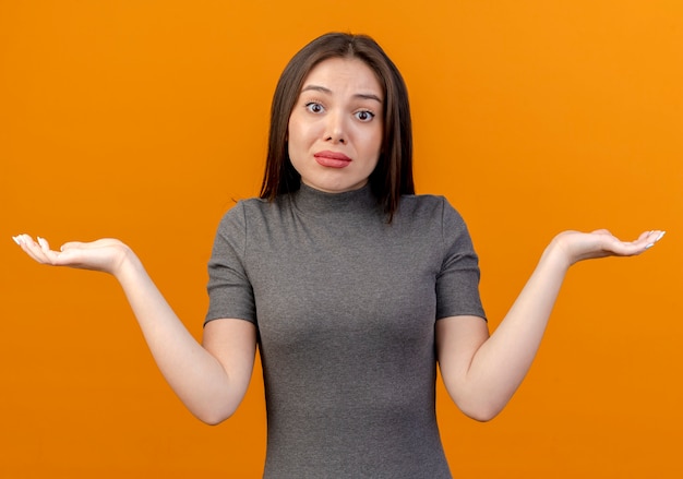 Free photo confused young pretty woman showing empty hands isolated on orange background