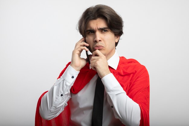 Confused young superhero guy looking at side wearing tie speaks on phone grabbed chin isolated on white