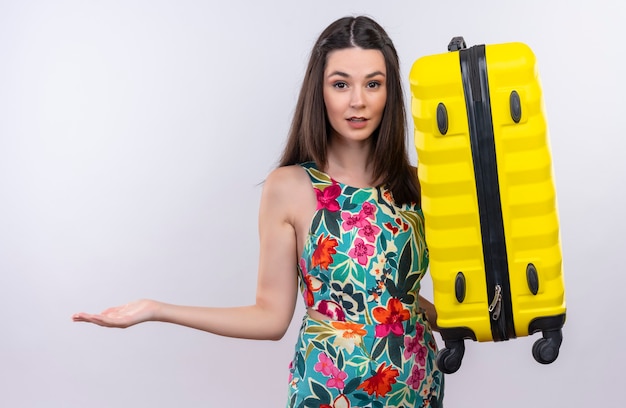 Путать молодой путешественник женщина, держащая чемодан на изолированной белой стене