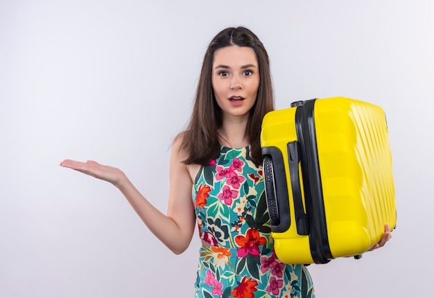 Confused young traveler woman holding suitcase on isolated white wall