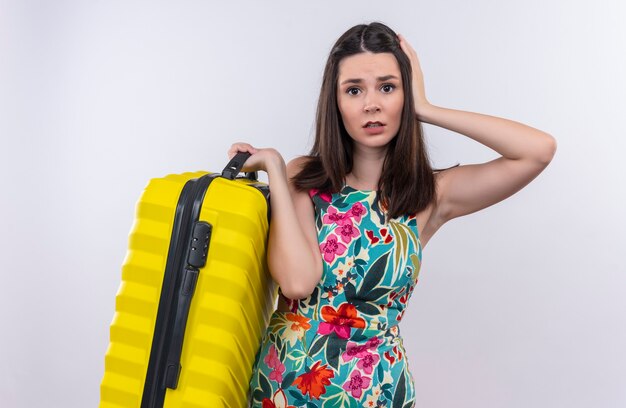 Confused young traveler woman holding suitcase standing over isolated white wall