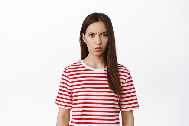 Confused young woman look puzzled, raise eyebrow and stare at something strange, confusing thing, standing puzzled against white background. Copy space