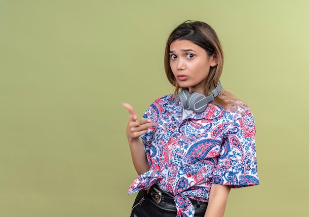 A confused young woman in paisley printed shirt wearing headphones smiling