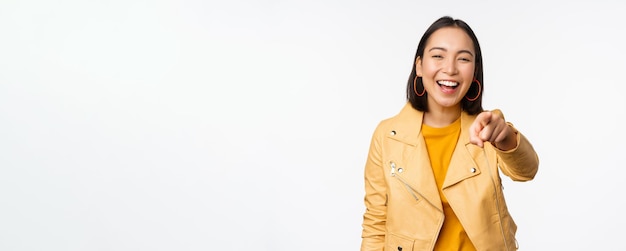 Congratulations its you Happy beautiful asian woman laughing pointing finger at camera choosing inviting people recruiting standing over white background