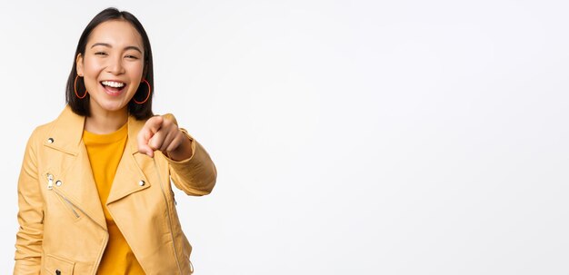 Congratulations its you Happy beautiful asian woman laughing pointing finger at camera choosing inviting people recruiting standing over white background