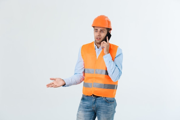 건설 엔지니어는 휴대전화로 이야기하고, 진지한 성인 남성은 스마트폰을 사용하여 건설 현장에서 일하는 사람들과 의사소통을 합니다.