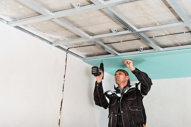 Free photo construction worker assembly suspended ceiling with drywall and fixing the drywall to the ceiling metal frame with screwdriver.