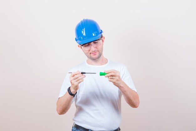 Construction worker fixing screwdriver in t-shirt, jeans, helmet and looking careful