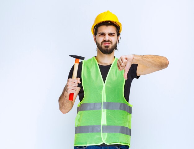 Рабочий-строитель держа молоток и показывая большой палец вниз знак.