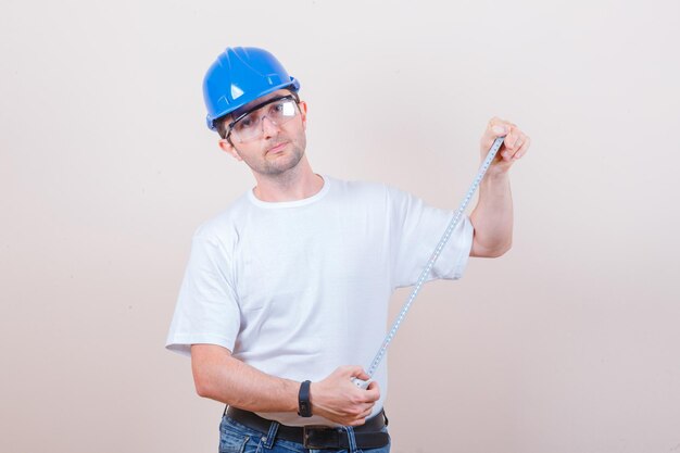 Construction worker holding measuring tape in t-shirt, jeans and helmet and looking confident