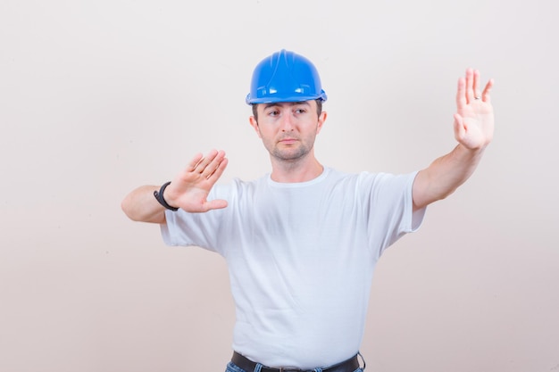 Строитель держит руки, чтобы защитить себя в футболке, джинсах, шлеме и выглядит решительным