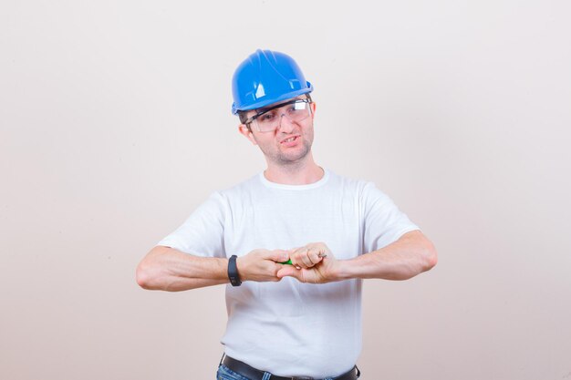 Construction worker squeezing screwdriver in t-shirt, jeans, helmet