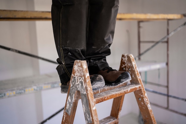 Free photo construction worker standing on dirty ladder