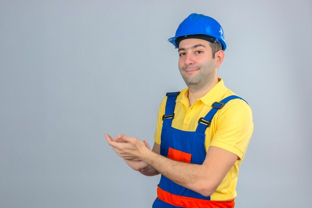 白で隔離される顔に笑顔で拍手制服と青の安全ヘルメットの建設労働者