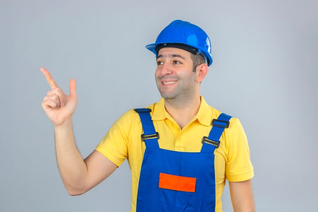 白で隔離される指で上向きの幸せそうな顔で制服と青い安全ヘルメットの建設労働者