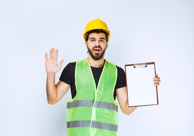 Рабочий-строитель с желтым шлемом, держащим отчет о проекте.