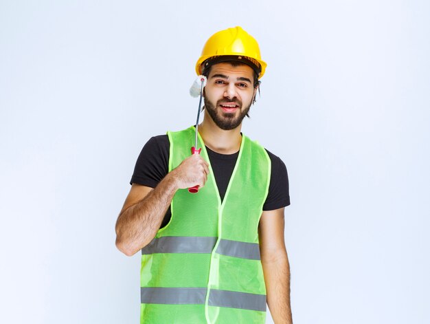 Construction worker with a yellow helmet holding a white trim roller.