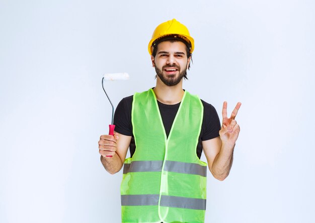 Construction worker with a yellow helmet holding a white trim roller.