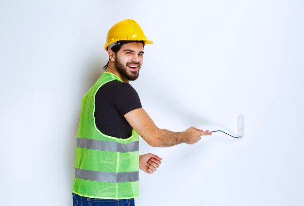 トリムローラーで白い壁を描いている黄色いヘルメットを持つ建設労働者。