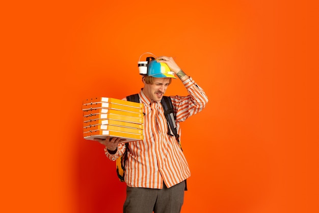 Contacless delivery service during quarantine. Man delivers food and shopping bags during insulation. Emotions of deliveryman isolated on orange background.