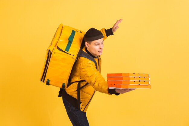 Contacless delivery service during quarantine man delivers food and shopping bags during insulation emotions of deliveryman isolated on yellow wall