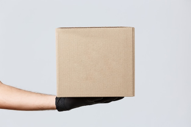 Contactless delivering, covid-19 and shopping concept. Image of courier hand in rubber gloves holding package, box with client order. Delivery guy handing out parcel to customer