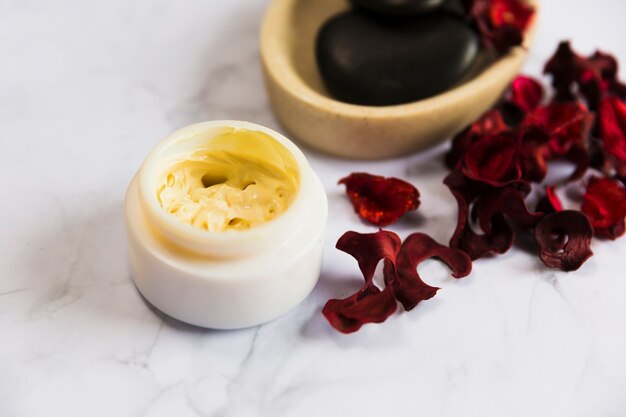 Container of cosmetic moisturizing cream with red orchid petals