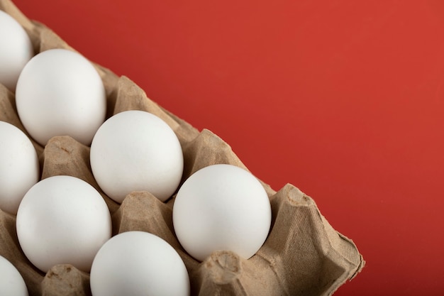 Container of white eggs on red surface. 