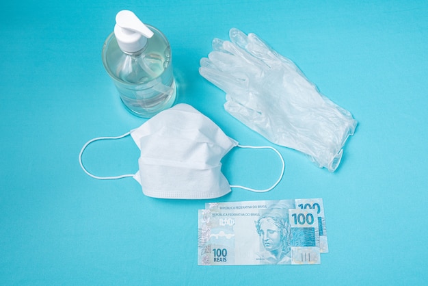 Container with alcohol gel, gloves, surgical mask and brazilian real money, 