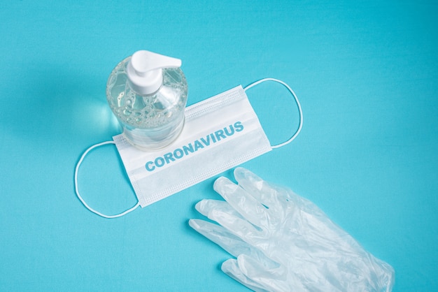 Container with alcohol gel, gloves and surgical mask on the light blue wall