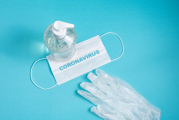 Container with alcohol gel, gloves and surgical mask on the light blue wall