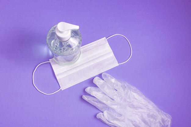 container with alcohol gel, gloves and surgical mask on the light blue