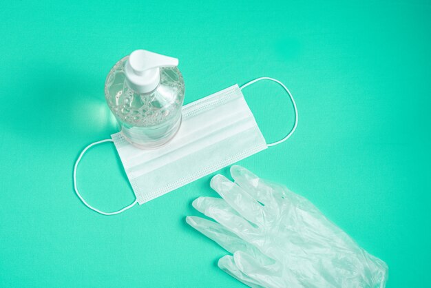 Container with alcohol gel, gloves and surgical mask on the light blue