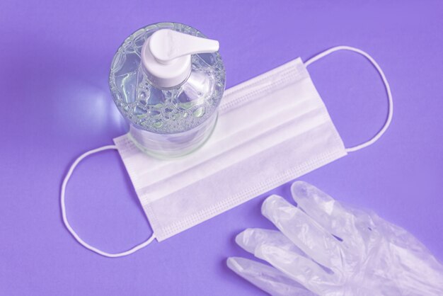 Container with alcohol gel, gloves and surgical mask on the light blue
