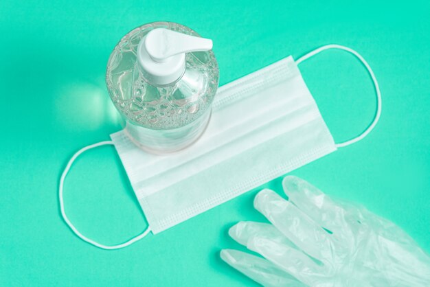 container with alcohol gel, gloves and surgical mask on the light blue
