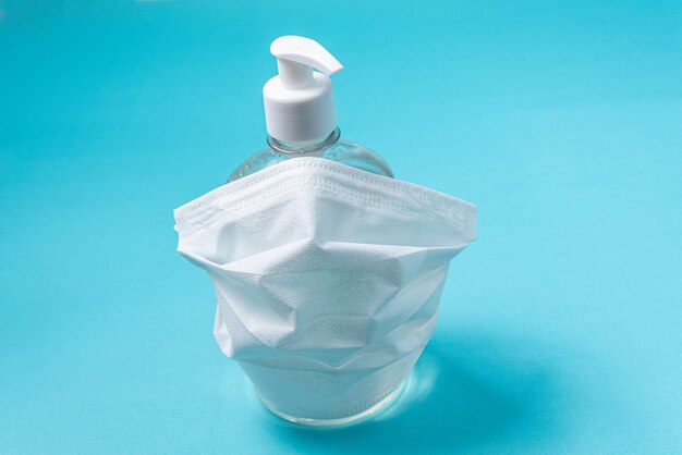 container with alcohol gel and surgical mask on the light blue