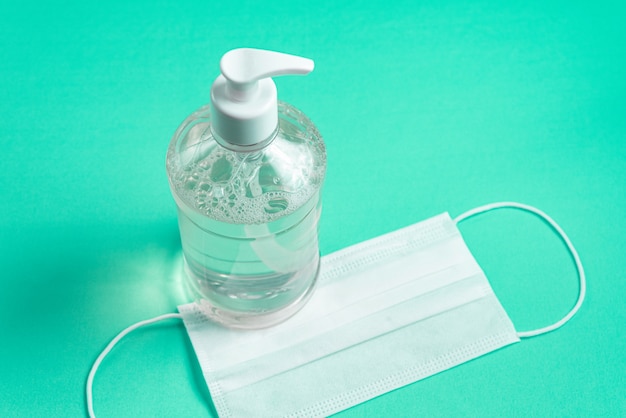 Container with alcohol gel and surgical mask on the light blue