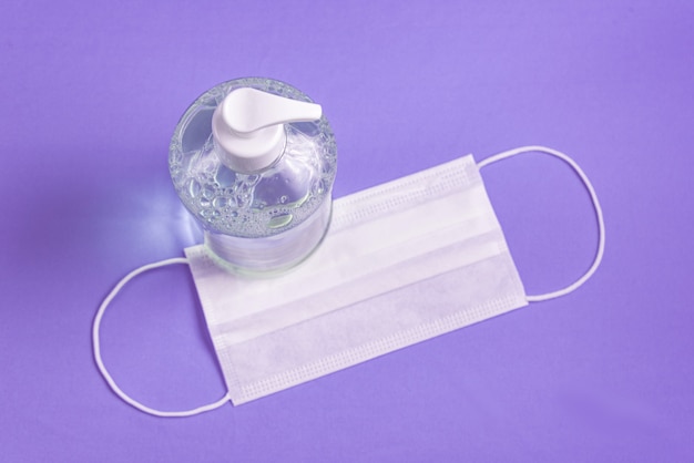 container with alcohol gel and surgical mask on the light blue