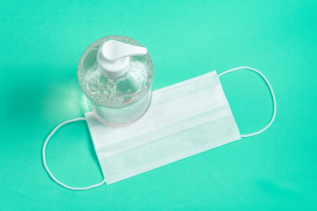 container with alcohol gel and surgical mask on the light blue