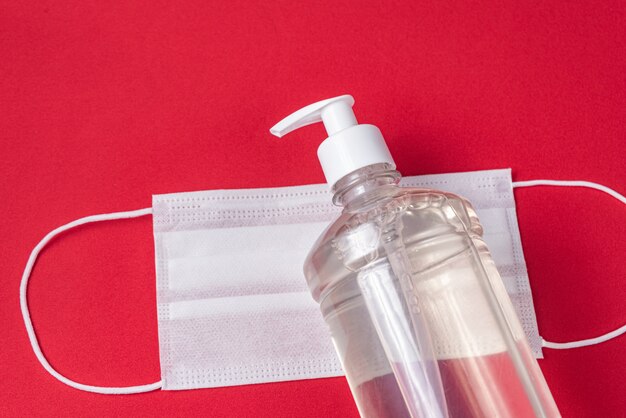 Container with alcohol gel and surgical mask on the red wall