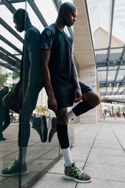 Contemplated african young male athlete leaning on reflective mirror at outdoors