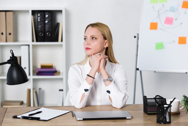 Contemplated blonde young businesswoman sitting at workplace in the office