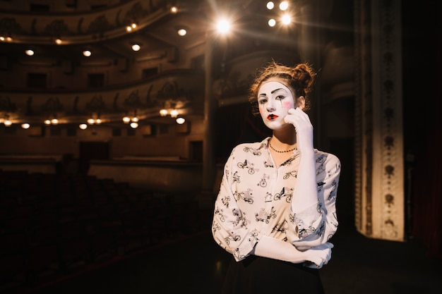 Contemplated female mime standing on stage in auditorium