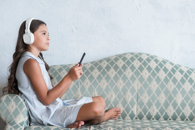 Contemplated girl sitting on sofa listening music on headphone