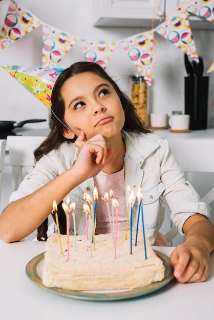 Contemplated girl with her birthday cake at home