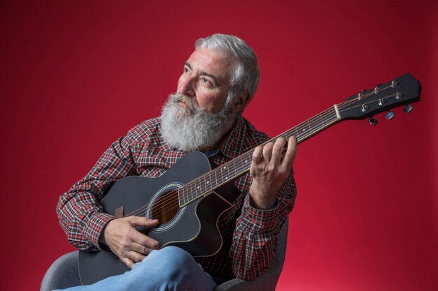 Contemplated senior man playing guitar against red background