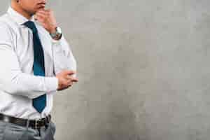 Free photo contemplated young businessman in formalwear standing against grey concrete wall