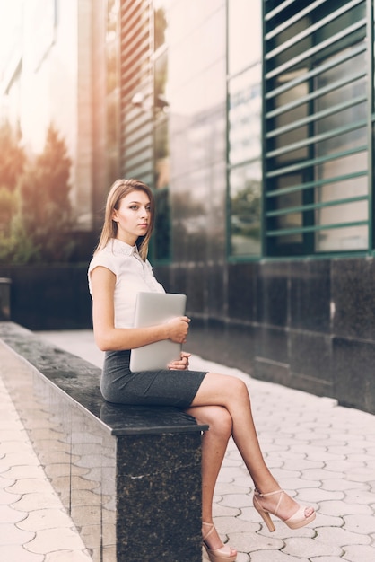 Contemplated young businesswoman holding digital tablet sitting on marble bench